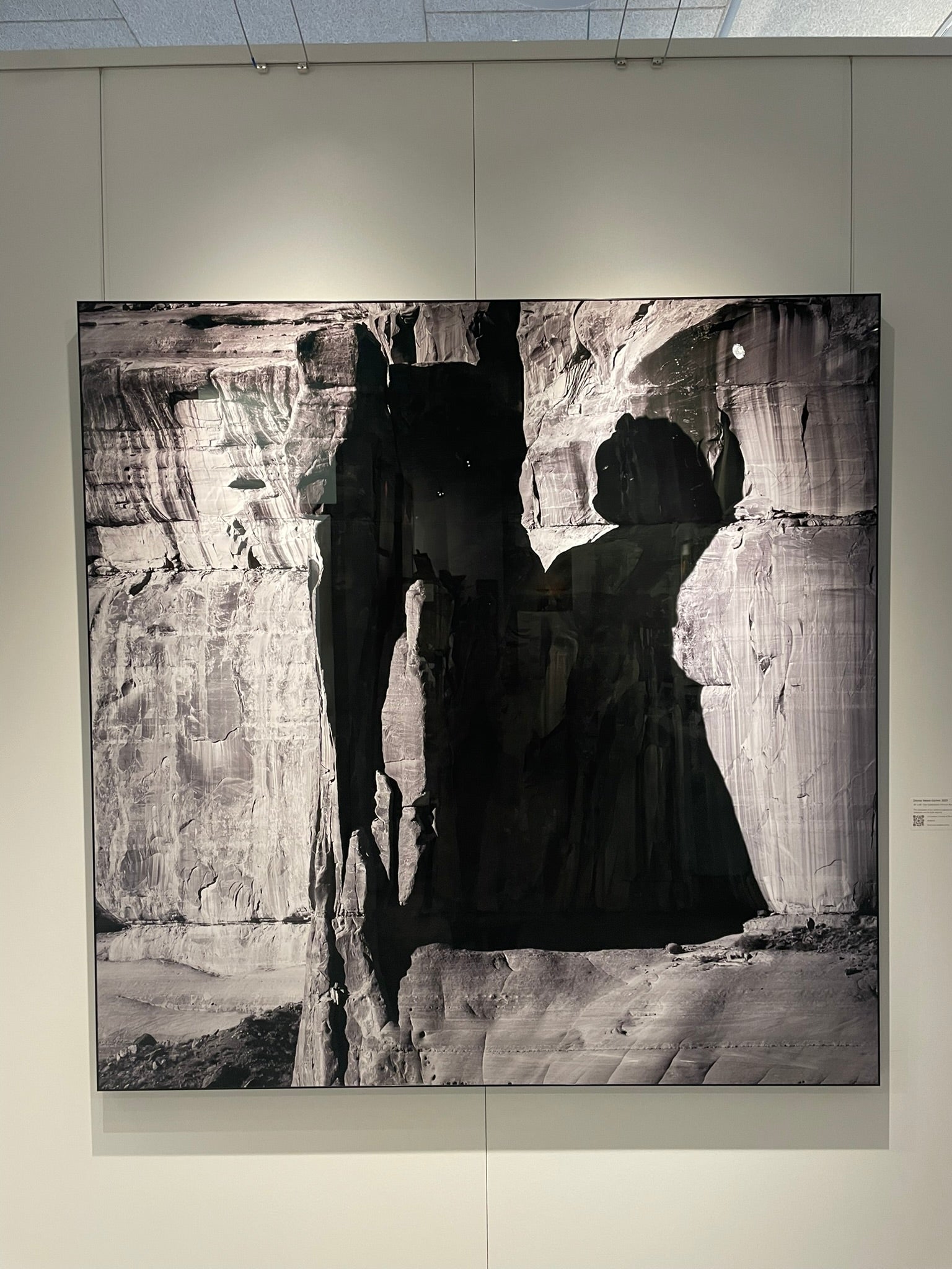 Black and white photograph of a person in a dark coat standing in front of a rocky landscape.