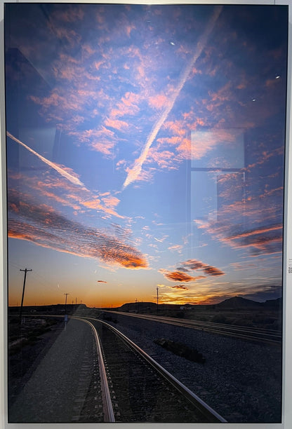 Sunset over a desert landscape with railway tracks and power lines.