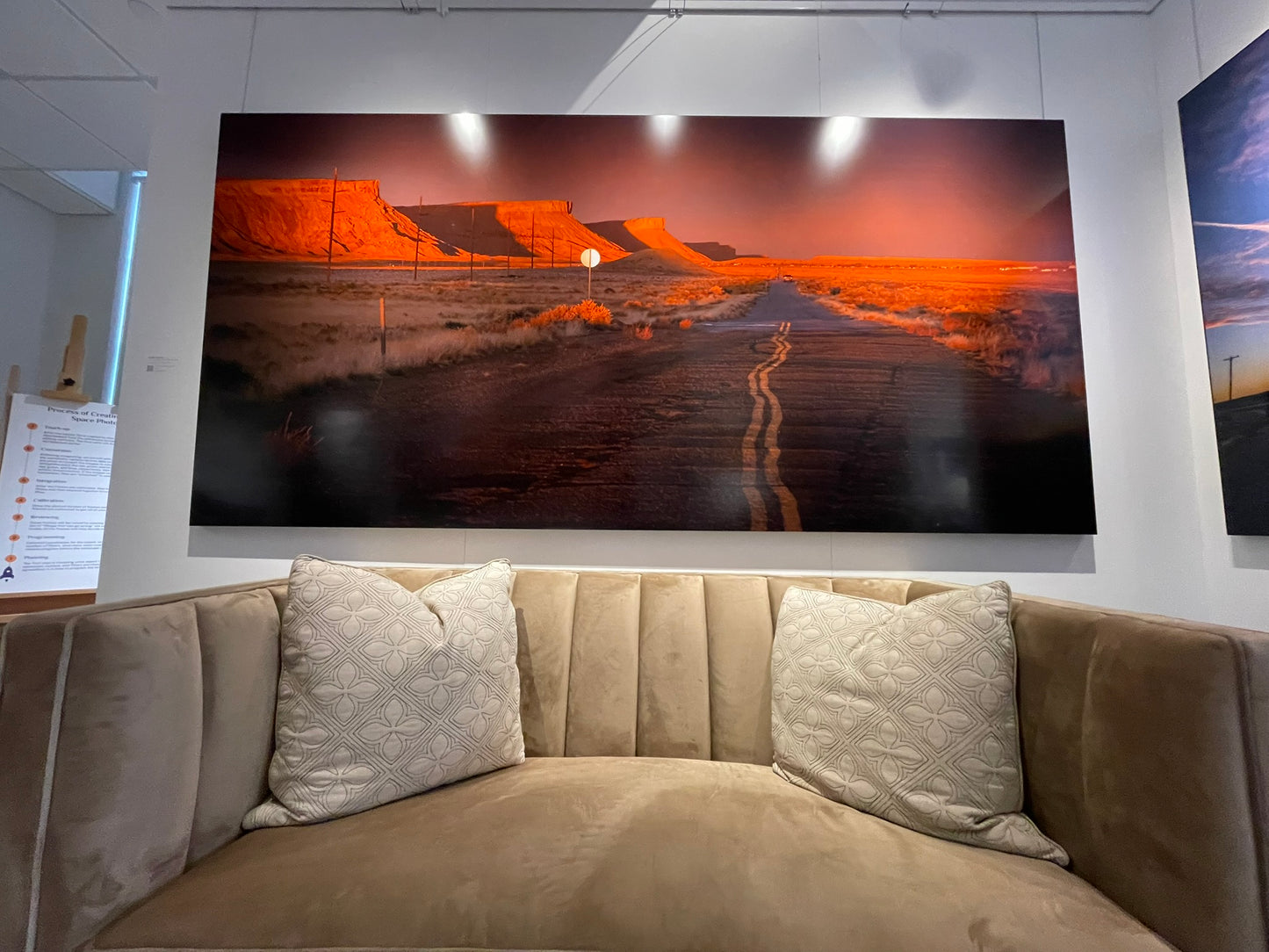 Large wall art of a desert landscape with a road and person in the distance, displayed in a room with a beige sofa.