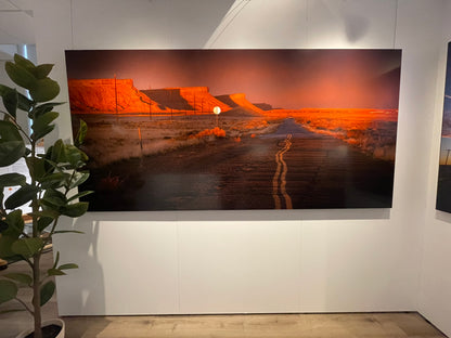 Large artwork of a desert road with orange cliffs on a white wall.