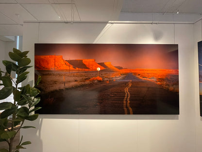 Large landscape painting of a desert scene with orange and brown hues on a white wall.