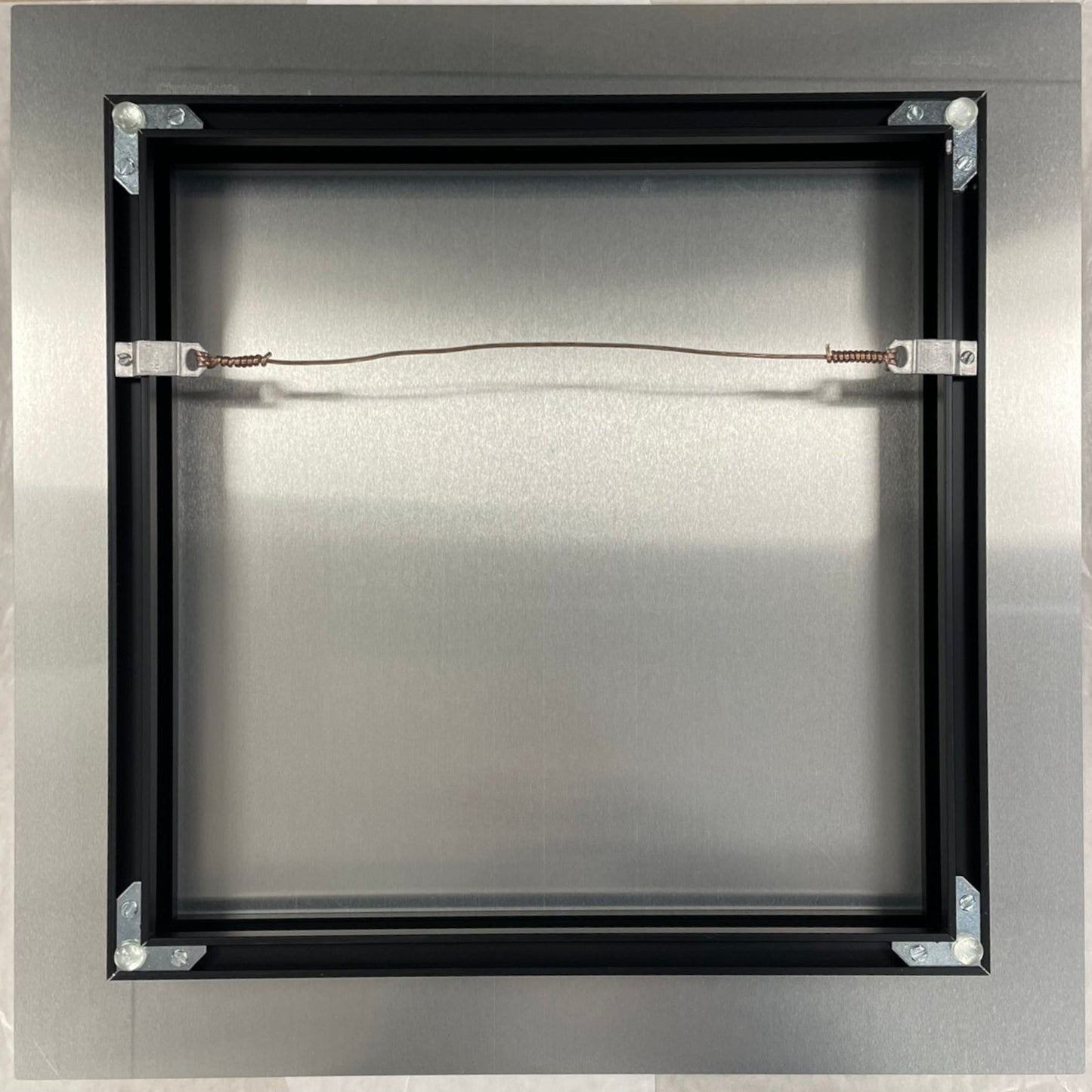 Metallic square object with a central wire on a beige background