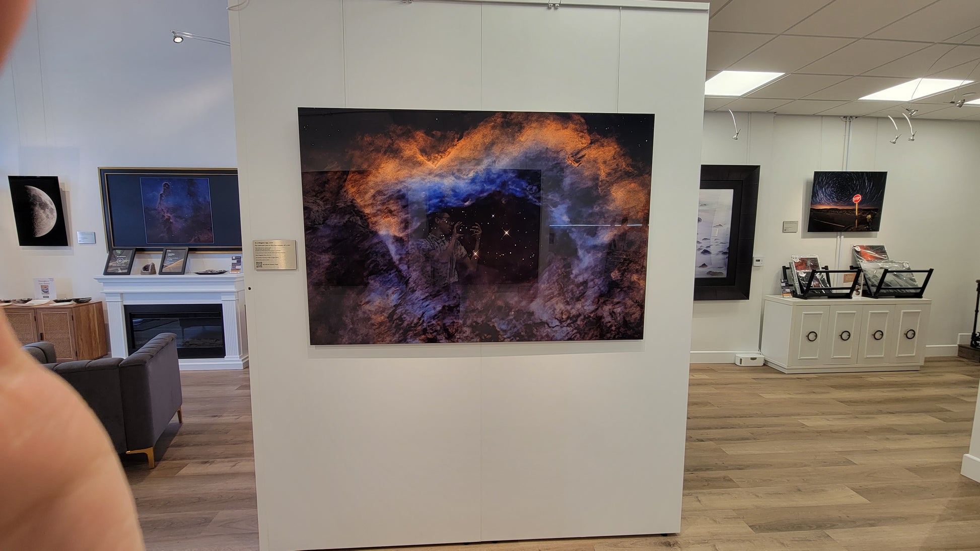 A photograph of the gallery interior showing the metal print titled "In A Dragon's Eye" on display. Other metal prints in view include "1st Quarter Moon" and "Strange Occurrences in the Desert".