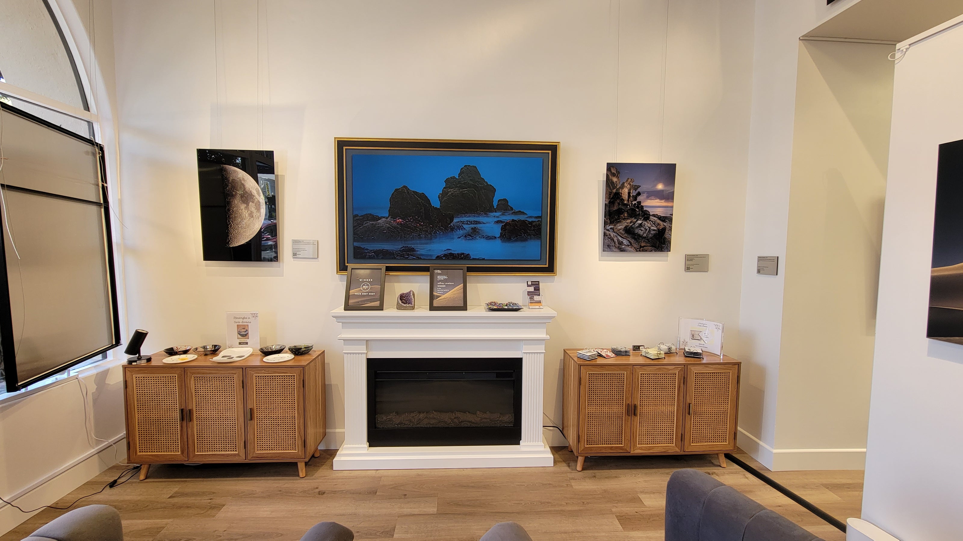 A photograph of the gallery interior facing the fireplace showing the metal prints titled "1st Quarter Moon" and "The Ancient Mariner" on display opposite the tv, which is displaying the photograph titled "Seaing Stars".