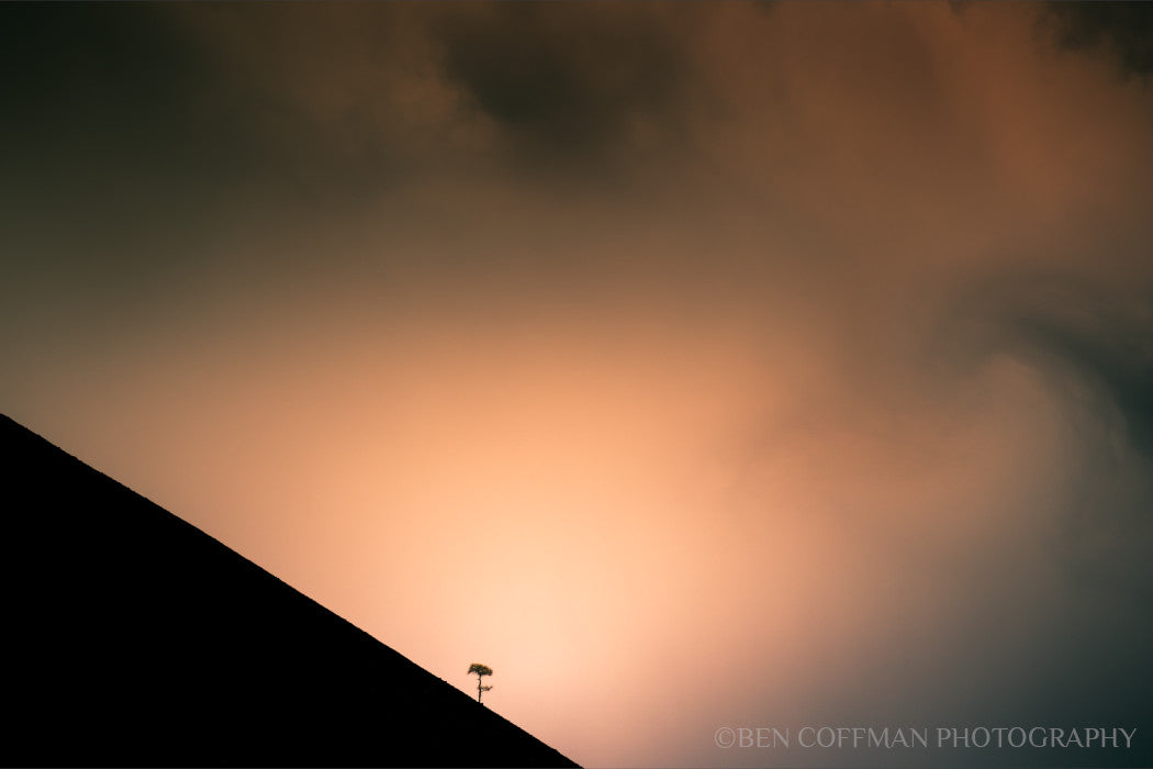 A jpg of the infrared photograph titled "Shadow Archetype" shot by landscape photographer Ben Coffman, featuring storm clouds swirling over a lone tree on the side of a cinder cone volcano, infrared, Lassen Volcanic National Park, California.