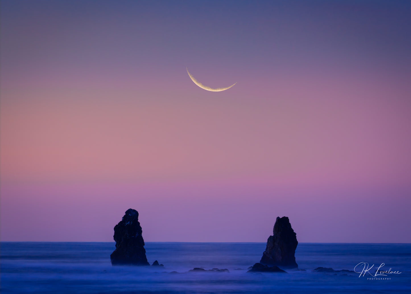 A jpg of the photograph titled "That Dream I Had" shot by landscape photographer J K Lovelace, featuring two figure-like rock formations facing a crescent moon against a surreal sunset.