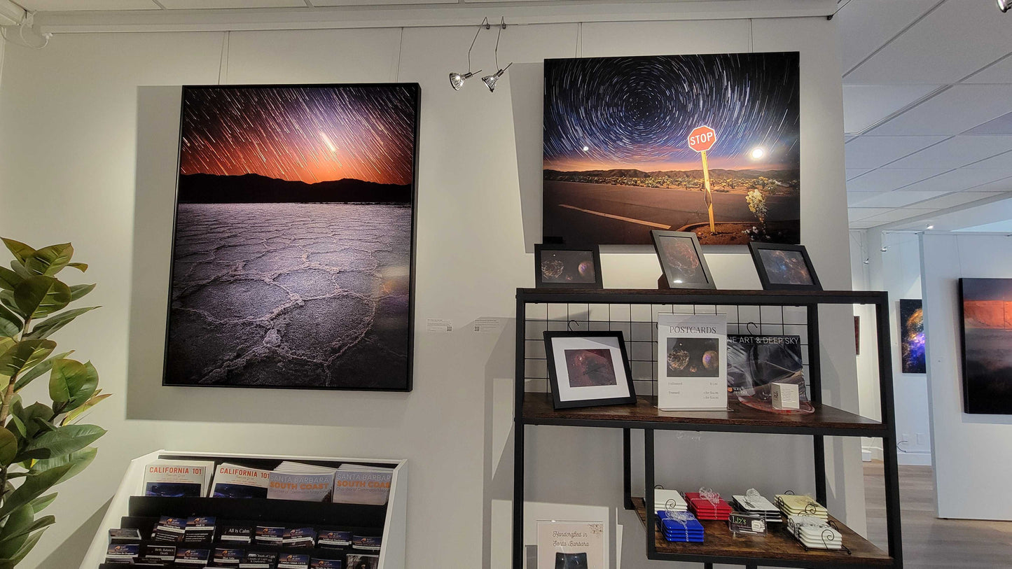 A photograph of the interior of Slice of Light Gallery taken from the vantage point of the gift shop facing two metal prints titled "When Beginnings End" and  "Strange Occurrences in the Desert".
