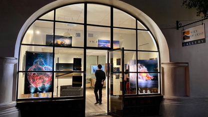 Person standing in front of a glass door with displayed artwork inside a gallery.