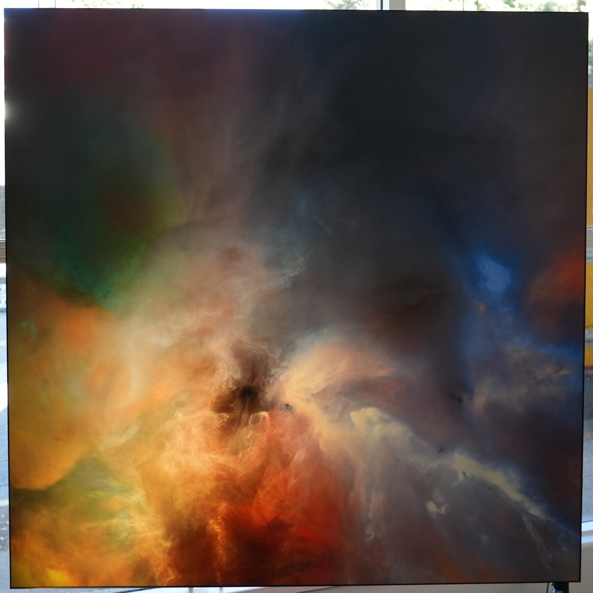 Framed space nebula artwork displayed in a room with a window showing an outdoor view.