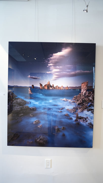 Large wall art of a coastal scene with rocks and water on a white wall.