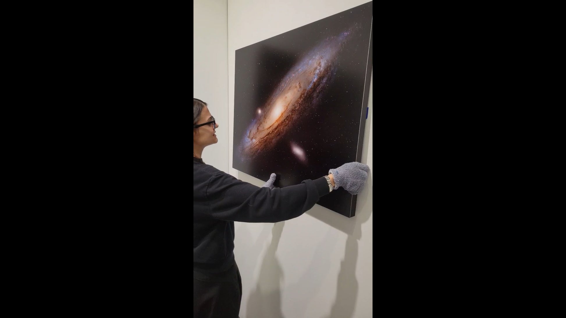 Person adjusting a large poster of a galaxy on a wall