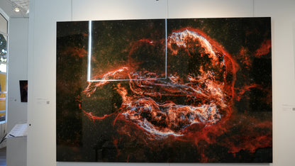 Artistic depiction of a cosmic scene with red and orange hues on a dark background, displayed in an art gallery.
