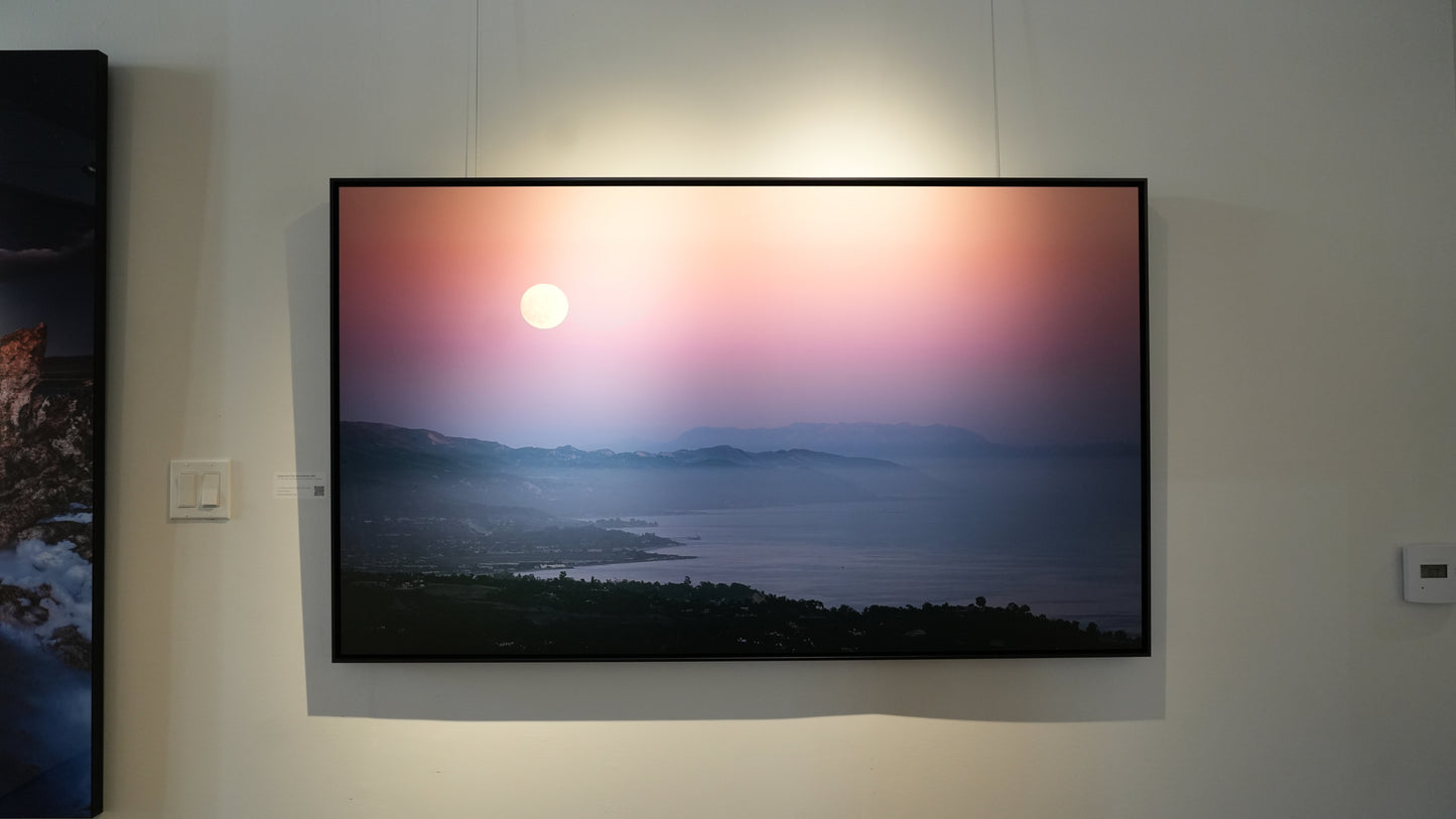 Framed photograph of a sunset over a mountain landscape on a wall.