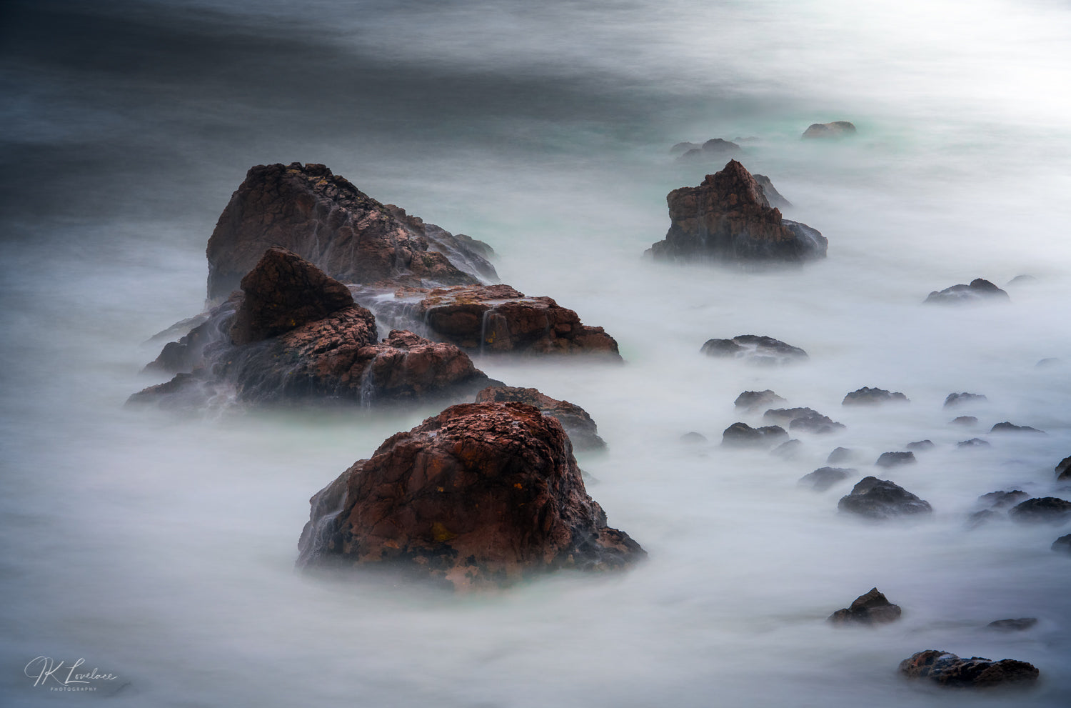 A jpg of the seascape photograph titled "Beyond Here Be Dragons" shot by landscape photographer J K Lovelace featuring coastal boulders in seawater.